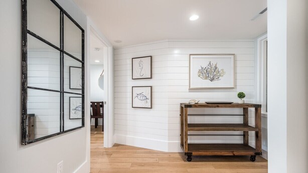 A hallway with wooden flooring, white walls, and a wooden cart with shelves. - MyStay at 1208 Villamare • Ocean views • Premier Design • New Pools & Hot Tubs! (Hilton Head Island)