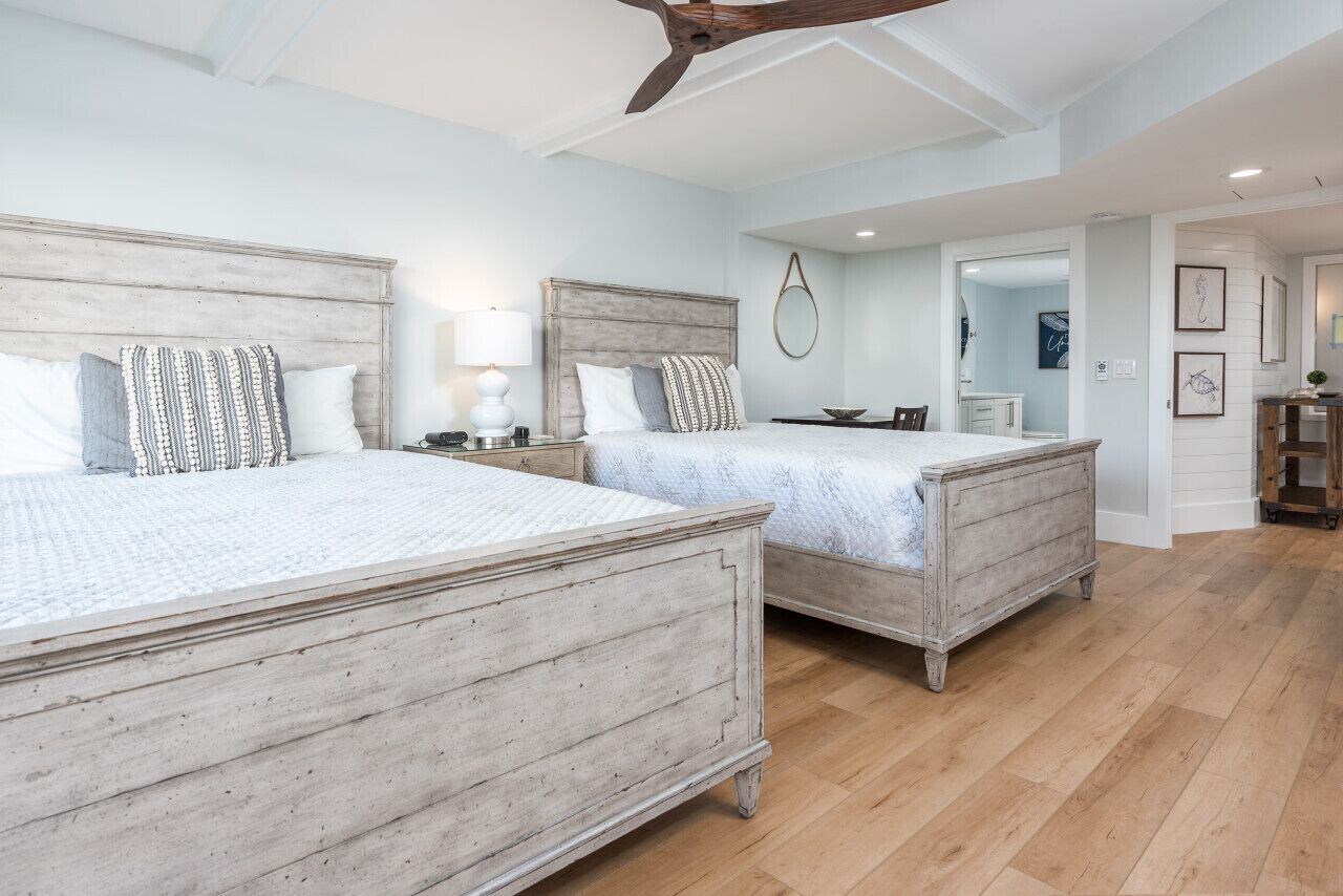 A bedroom with two wooden beds, a ceiling fan, and a small table with a lamp.