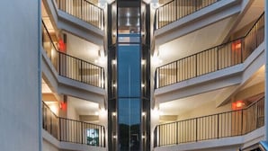 En modern byggnad med flera våningar, en central hisschakt och utomhusområden med sittplatser.