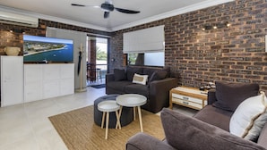 A modern living room with a brick wall, a flat-screen TV, a ceiling fan, and a sofa with a coffee table. - Sheridan by the Seashore (BONGAREE)