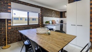A kitchen with a wooden table, chairs, and a window with a view of buildings. - Sheridan by the Seashore (BONGAREE)