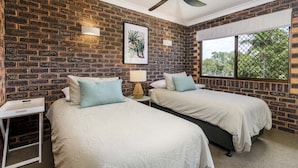 A room with two beds, a small table, a lamp, and a window with a view of trees. - Sheridan by the Seashore (BONGAREE)