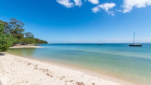 A beach with clear water, a sandy shore, and sailboats in the distance.