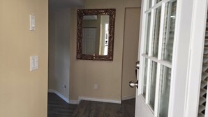 Un pasillo con paredes beige, suelo de madera, una puerta con panel de vidrio y un espejo decorativo en la pared.