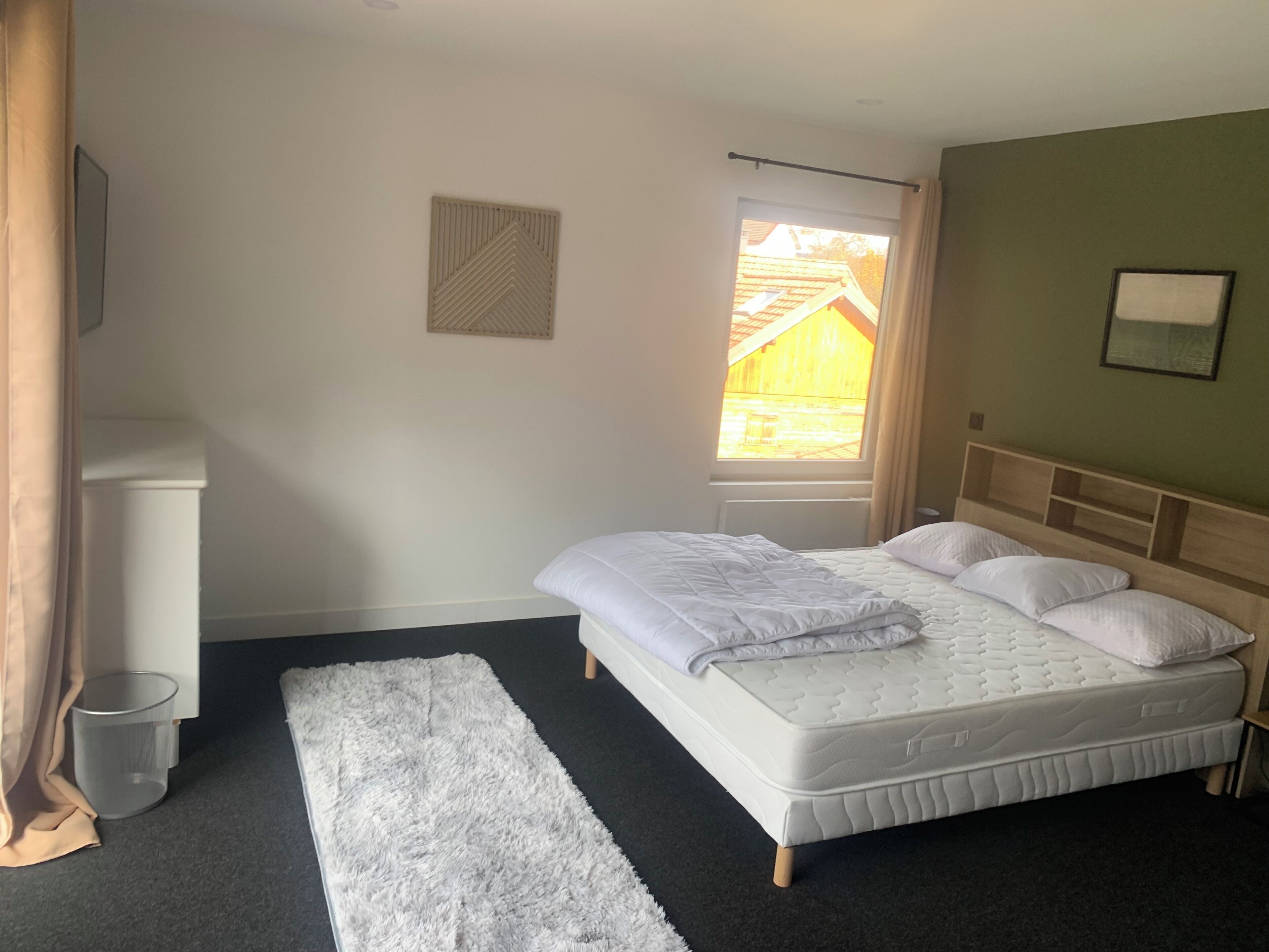 A bedroom with a bed, a window, a radiator, a white rug, and a wall-mounted picture.