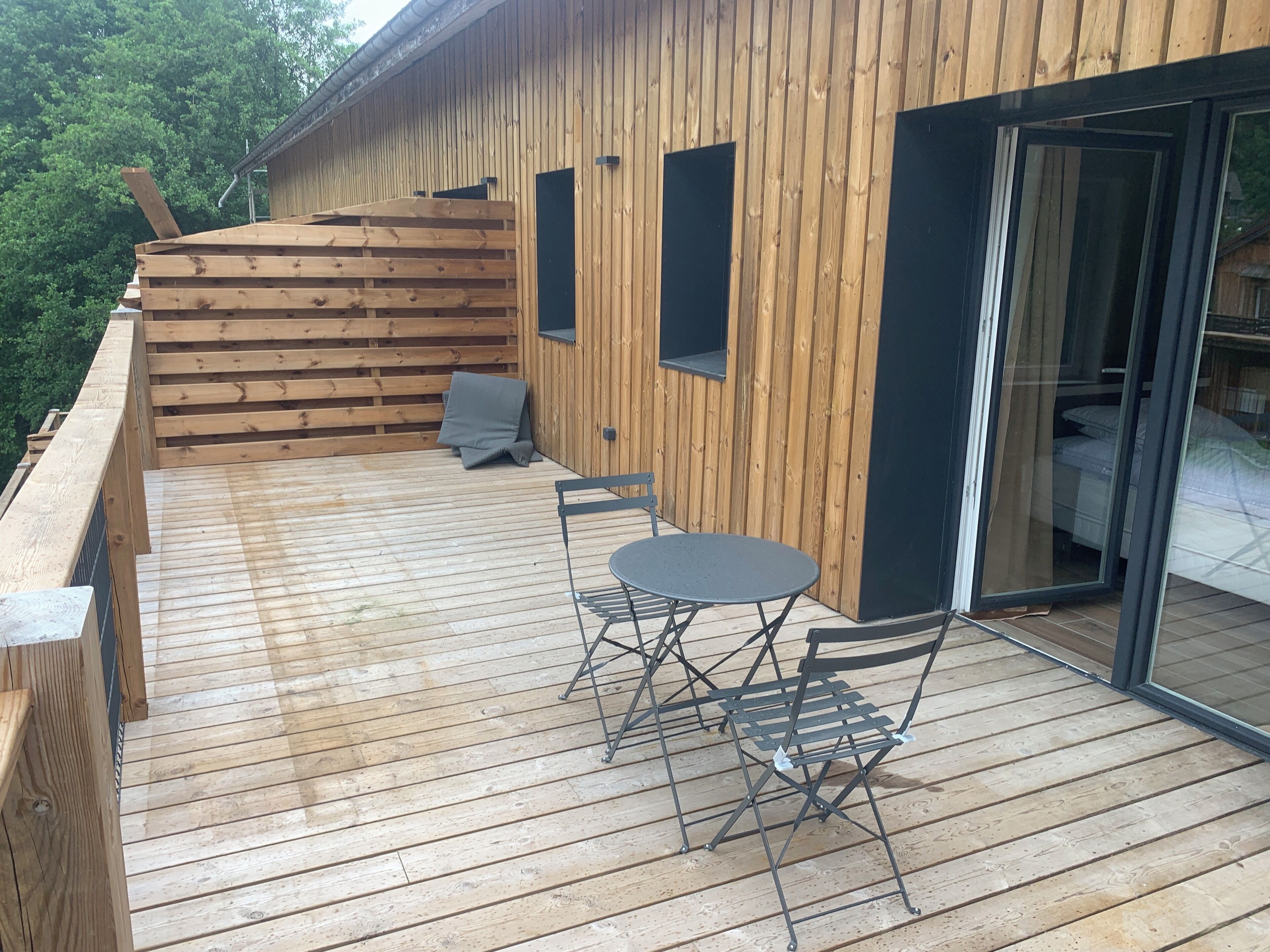 Een houten terras met een tafel, stoelen, een schuifpui en een klein zitgedeelte buiten.