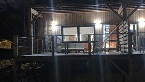 Ein Holzgebäude mit überdachter Terrasse, einer Treppe und einem umzäunten Grundstück.