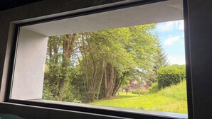Ein Fenster mit Blick auf eine bewaldete Landschaft und ein grünes Feld.