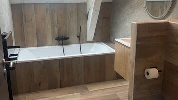 Een moderne badkamer met dakraam, houten vloer, een vrijstaand bad, toilet en spiegel.