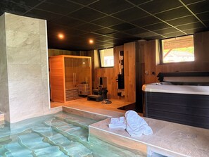 Un cuarto de spa con piso de vidrio, paredes de madera, sauna y tina de hidromasaje.
