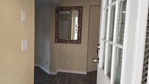 Un corridoio con pareti beige, pavimento in legno, una porta con un pannello di vetro e uno specchio decorativo appeso al muro.