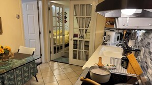 Een kleine keuken met een eethoek, met een kookplaat, pannen en een spoelbak.