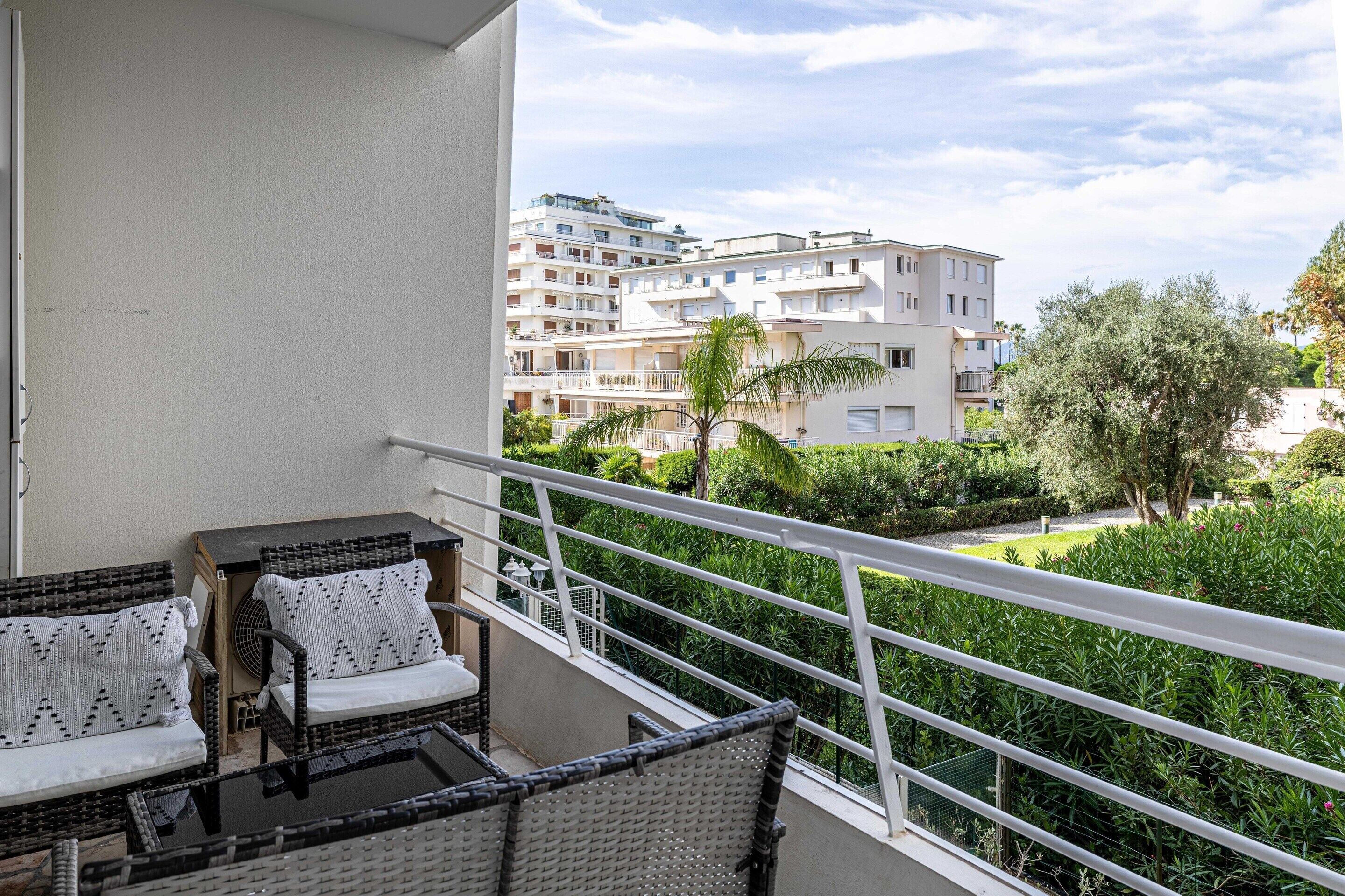 A balcony with wicker furniture and a view of residential buildings and greenery.
