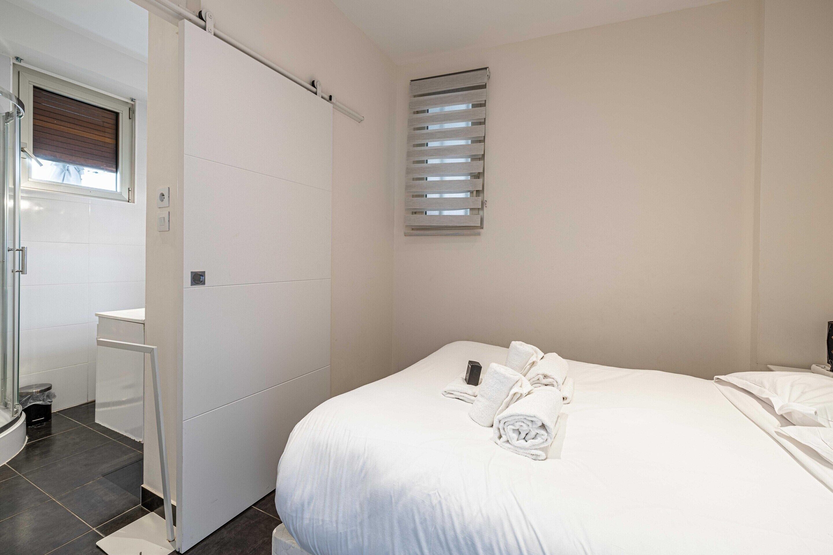 A hotel room with a bed, a bathroom, and a window with blinds.