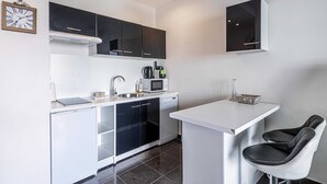 Een compacte keuken met witte kasten, een magnetron, een spoelbak en een klein barretje met twee stoelen.