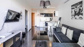 Een moderne woonkamer met een flatscreentelevisie, een bank en een eetgedeelte, met een keuken op de achtergrond.