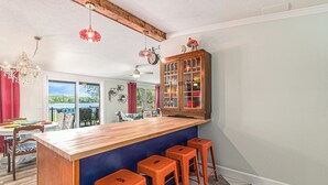 A kitchen with a wooden island, bar stools, a chandelier, and a view of the outdoors. - Wonderland: Waterfront + Game Room + Dog Friendly (Albion)