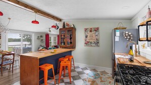 A kitchen with a wooden island, orange stools, a gas stove, and a refrigerator with magnets. - Wonderland: Waterfront + Game Room + Dog Friendly (Albion)