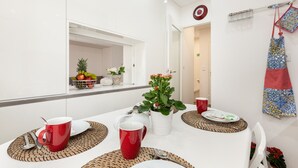 A dining area with a white table set for four, including red mugs, plates, and cutlery. A white vase with flowers and a fruit basket are on the table. - D&S - Torne Apartments II (Vila Nova de Gaia)
