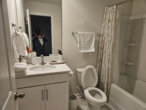 Een badkamer met toilet, wastafel en spiegel. Handdoeken hangen aan de muur en er is een douchegordijn.