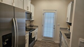 A compact kitchen with white cabinets, a stainless steel refrigerator, a microwave, and a built-in oven. - Family-Friendly 3BR Fast WiFi  10 Min to Uptown (Charlotte)