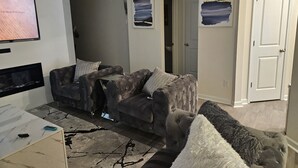 A living room with a grey sofa, a TV, a coffee table, and artwork on the walls. - Family-Friendly 3BR Fast WiFi  10 Min to Uptown (Charlotte)