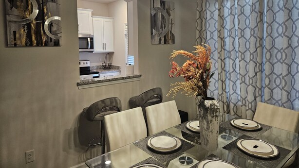 A dining area with a glass table, chairs, and a vase with dried flowers. - Family-Friendly 3BR Fast WiFi  10 Min to Uptown (Charlotte)