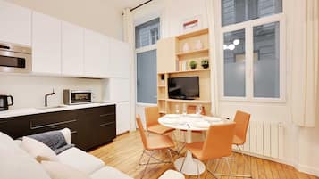 Une cuisine moderne avec des meubles blancs, un four à micro-ondes et une machine à café. Il y a également un coin repas avec une table, des chaises et un téléviseur.