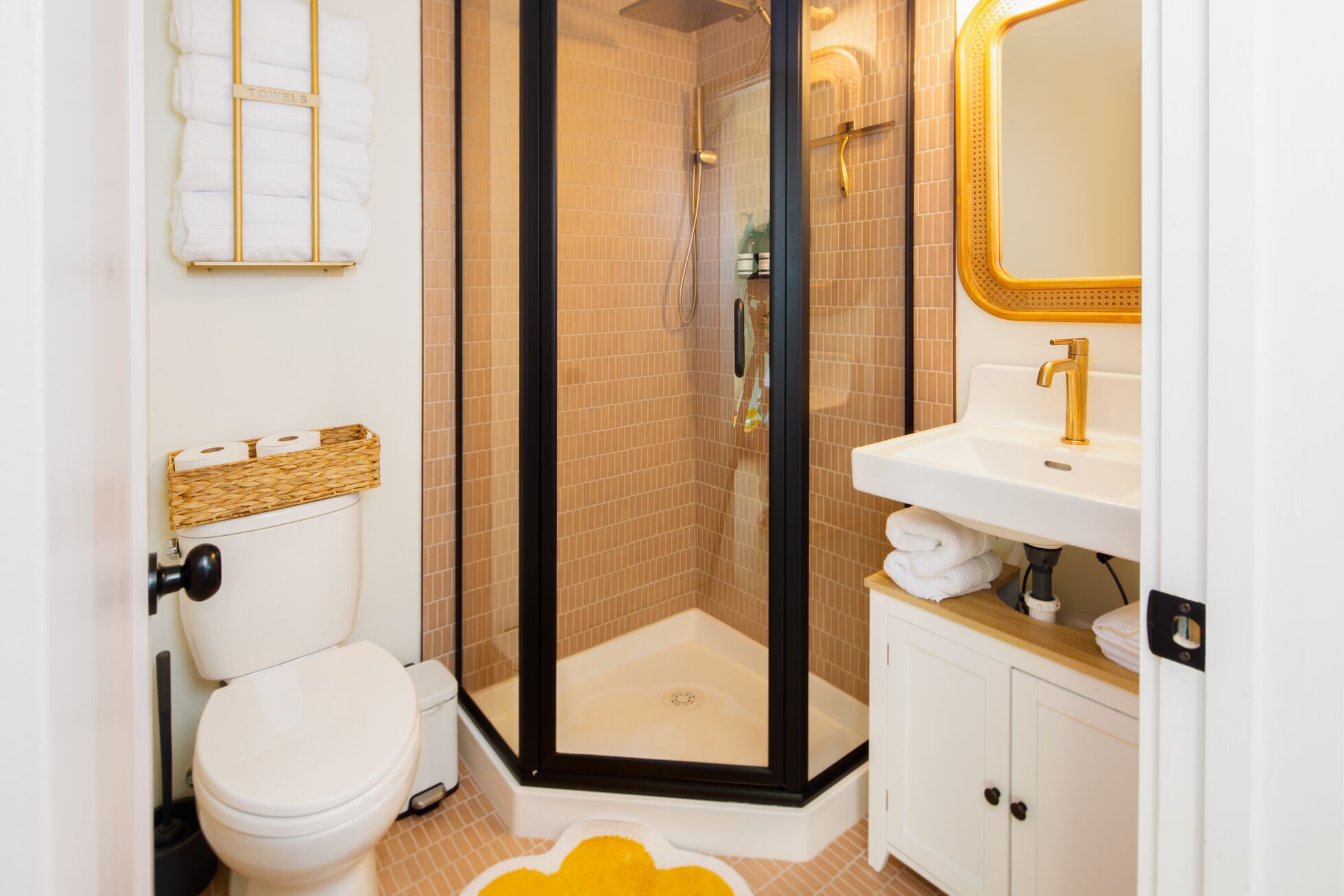 A bathroom with a toilet, a shower with a glass door, a sink with a gold faucet, and a mirror with a gold frame.