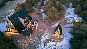 A modern lodge with a large central building and two smaller cabins, surrounded by a snowy landscape and dense trees. - A-Frame, HotTub, FirePit, Pergola, UFO Playscape, MiniAFrame ADU (Crestone)