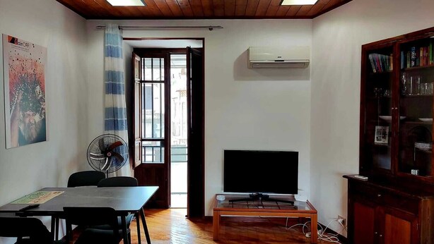 A room with a wooden ceiling, a TV on a stand, a dining table with chairs, and a cabinet with glass doors.