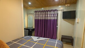 Ein Schlafzimmer mit Bett, Spiegel, Fernseher und einem violetten Vorhang.