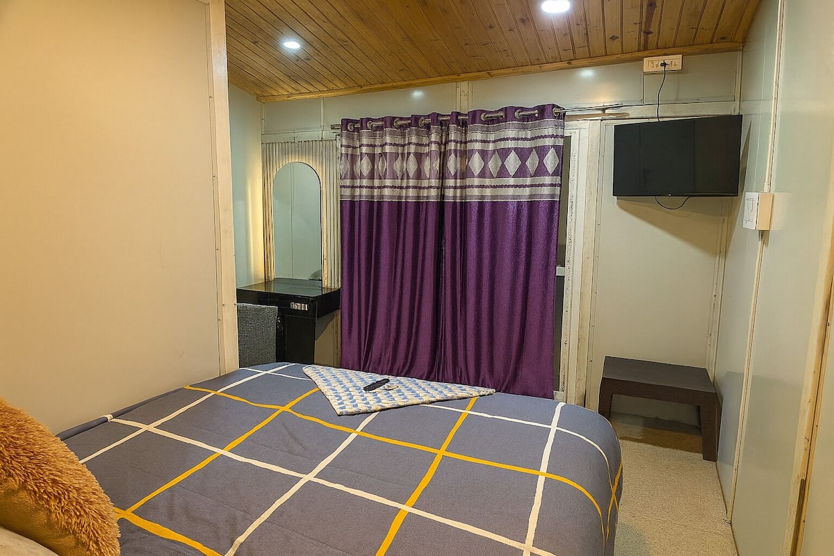 A bedroom with a bed, a mirror, a TV, and a purple curtain.