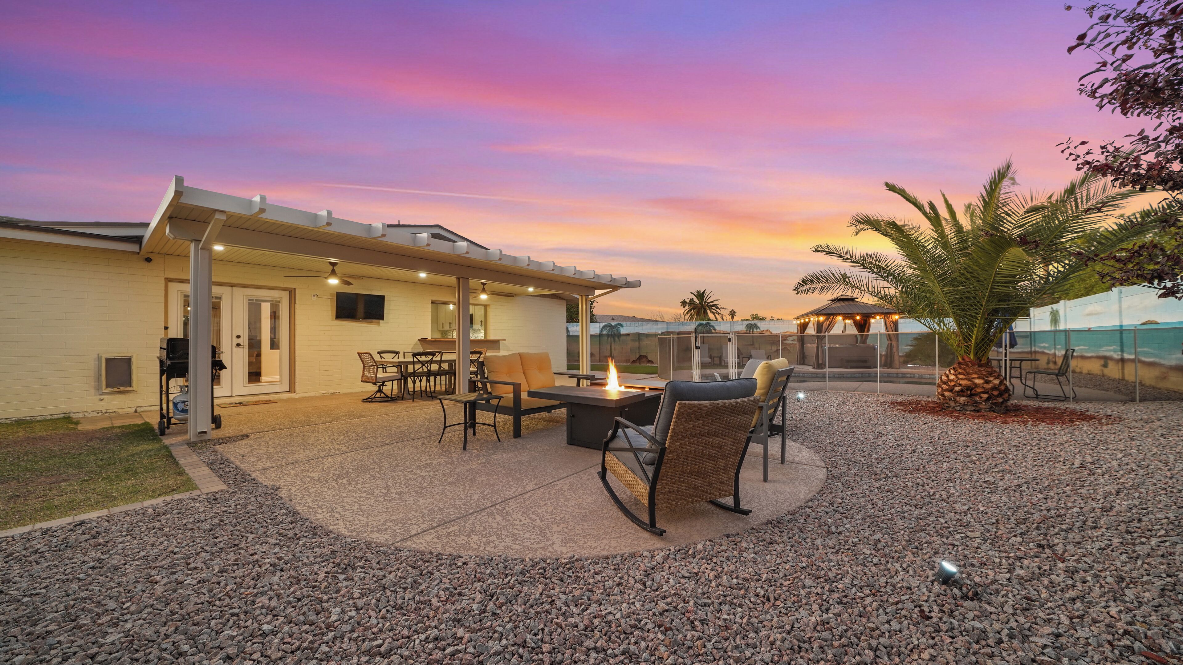 A patio with outdoor furniture, a fire pit, and a view of the ocean at sunset.