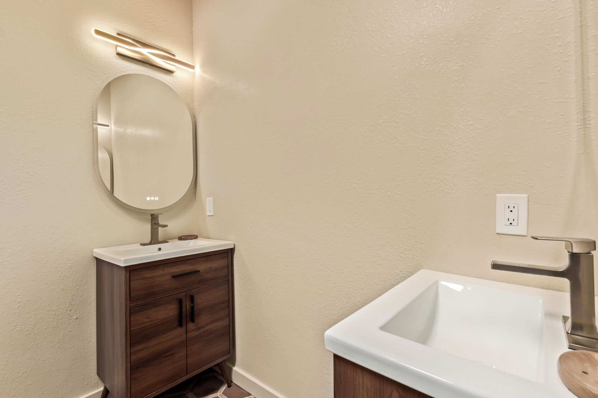 Een badkamer met een witte wastafel, een houten opbergmeubel, een ronde spiegel en een wandlamp.