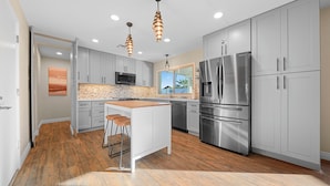 A modern kitchen with grey cabinets, stainless steel appliances, a wooden island with stools, and pendant lighting. - Unique 4-bed, 3-bath house with Pool, Hot Tub, Arcade and Hi-Spd Wifi (Tempe)