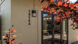 A building facade with a number '1956A' on the wall, a glass door entrance, and a patio area visible through the glass. - Unique 4-bed, 3-bath house with Pool, Hot Tub, Arcade and Hi-Spd Wifi (Tempe)