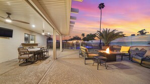 An outdoor patio with a dining area, a fire pit, and a view of the ocean at sunset. - Unique 4-bed, 3-bath house with Pool, Hot Tub, Arcade and Hi-Spd Wifi (Tempe)