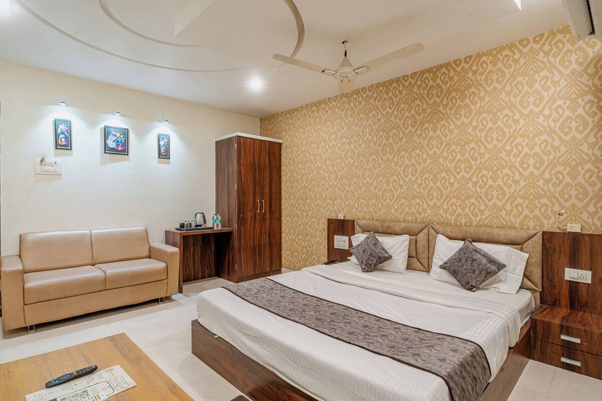 A bedroom with a bed, a wooden wardrobe, a sofa, and a ceiling fan.