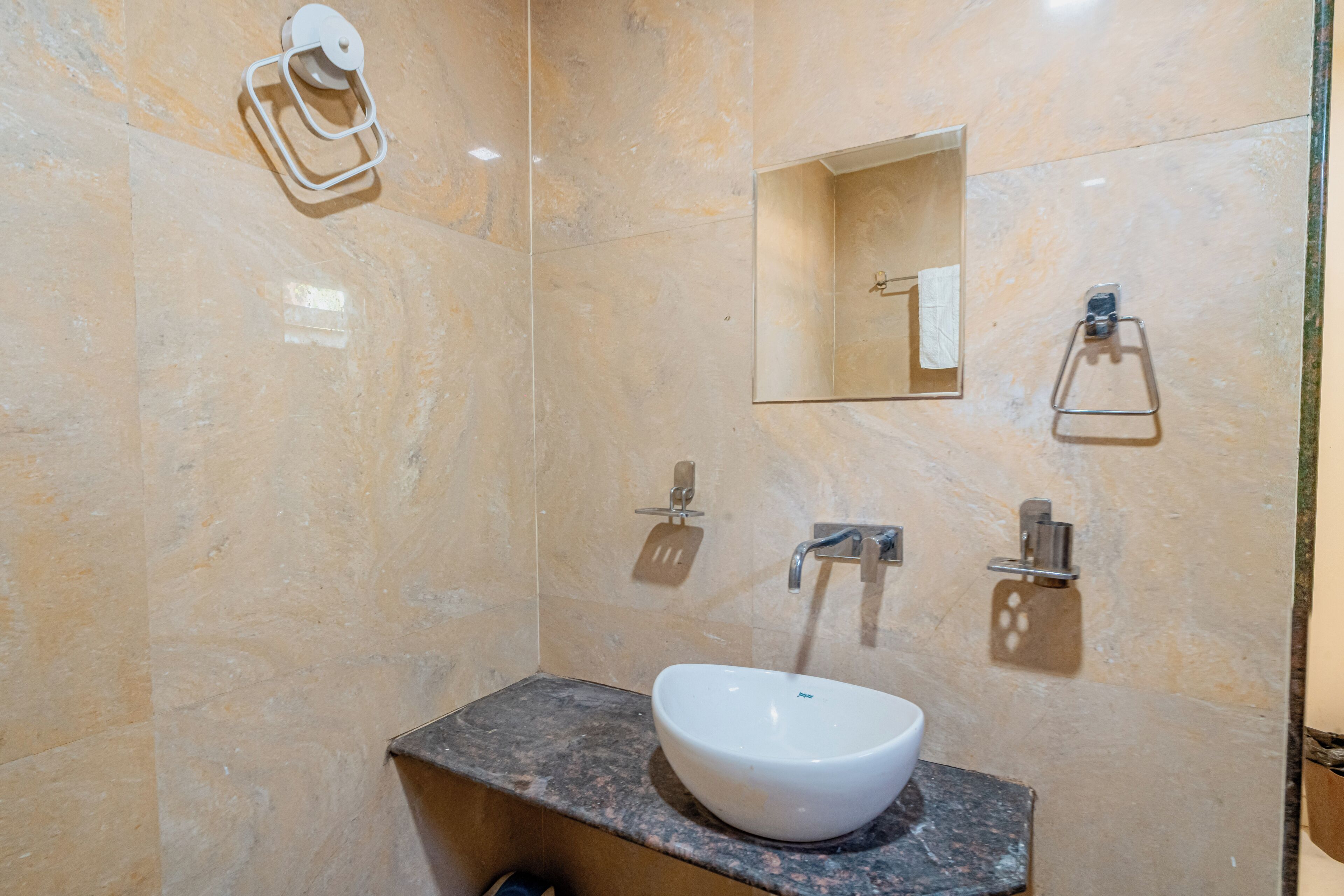 A bathroom with a marble wall, a sink with a marble countertop, a towel dispenser, a mirror, and a soap dispenser.