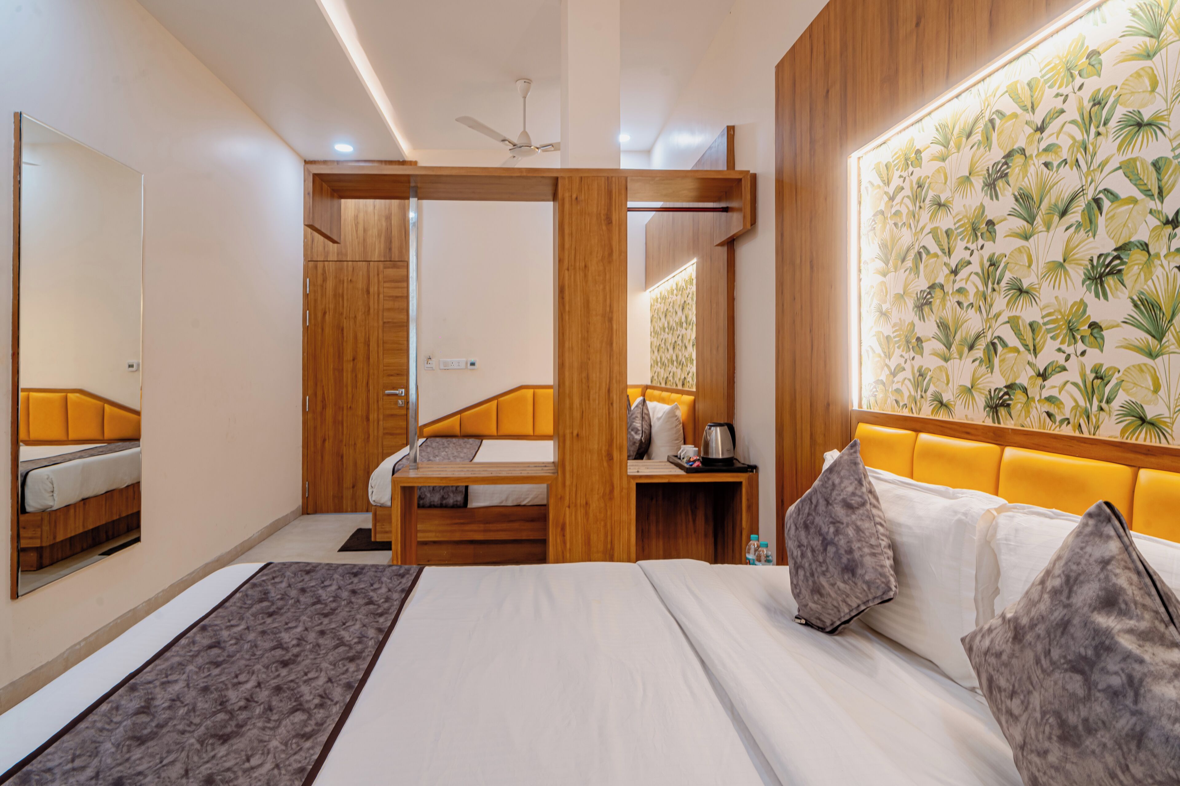 A modern hotel room with a large bed, a wooden wardrobe, a bedside table with a lamp, and a large mirror.