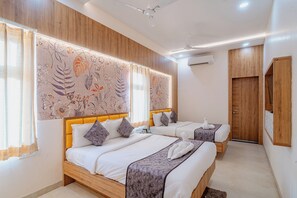 Une chambre d’hôtel avec deux lits, une tête de lit en bois, un grand mur orné d’un motif floral et un appareil de climatisation.