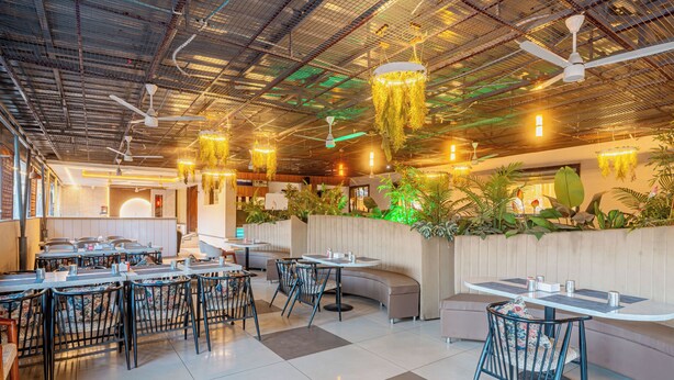 Un restaurante con varias zonas de estar, incluyendo mesas y cabinas, con plantas colgantes y ventiladores de techo.