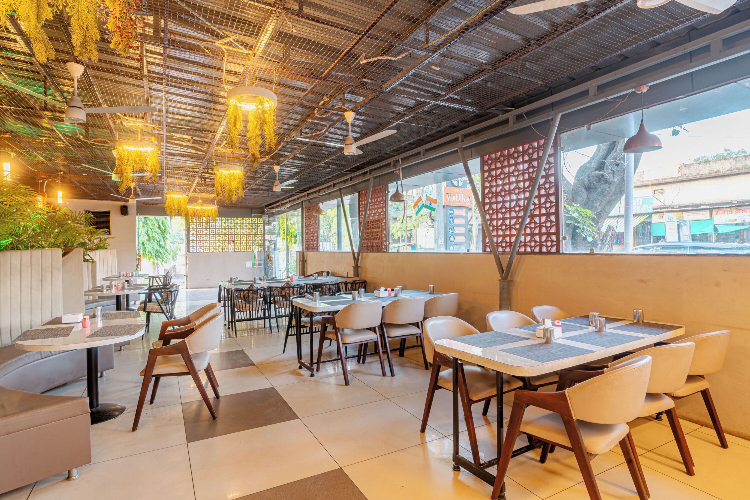 A restaurant interior with tables, chairs, hanging lights, and large windows.
