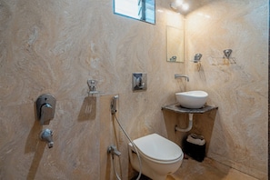 Une salle de bain avec un mur en marbre, des toilettes, un lavabo, une douche et un miroir.
