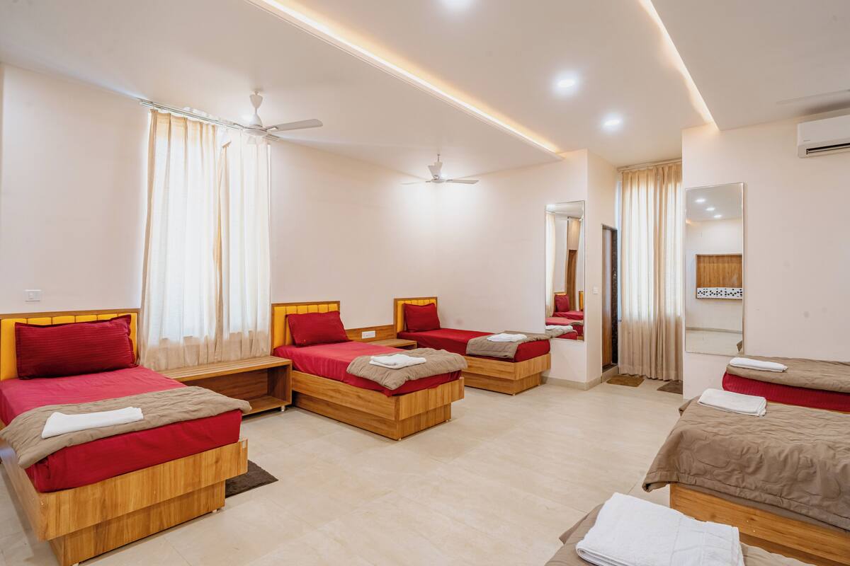 A hotel room with three wooden beds, a ceiling fan, a mirror, and an air conditioning unit.