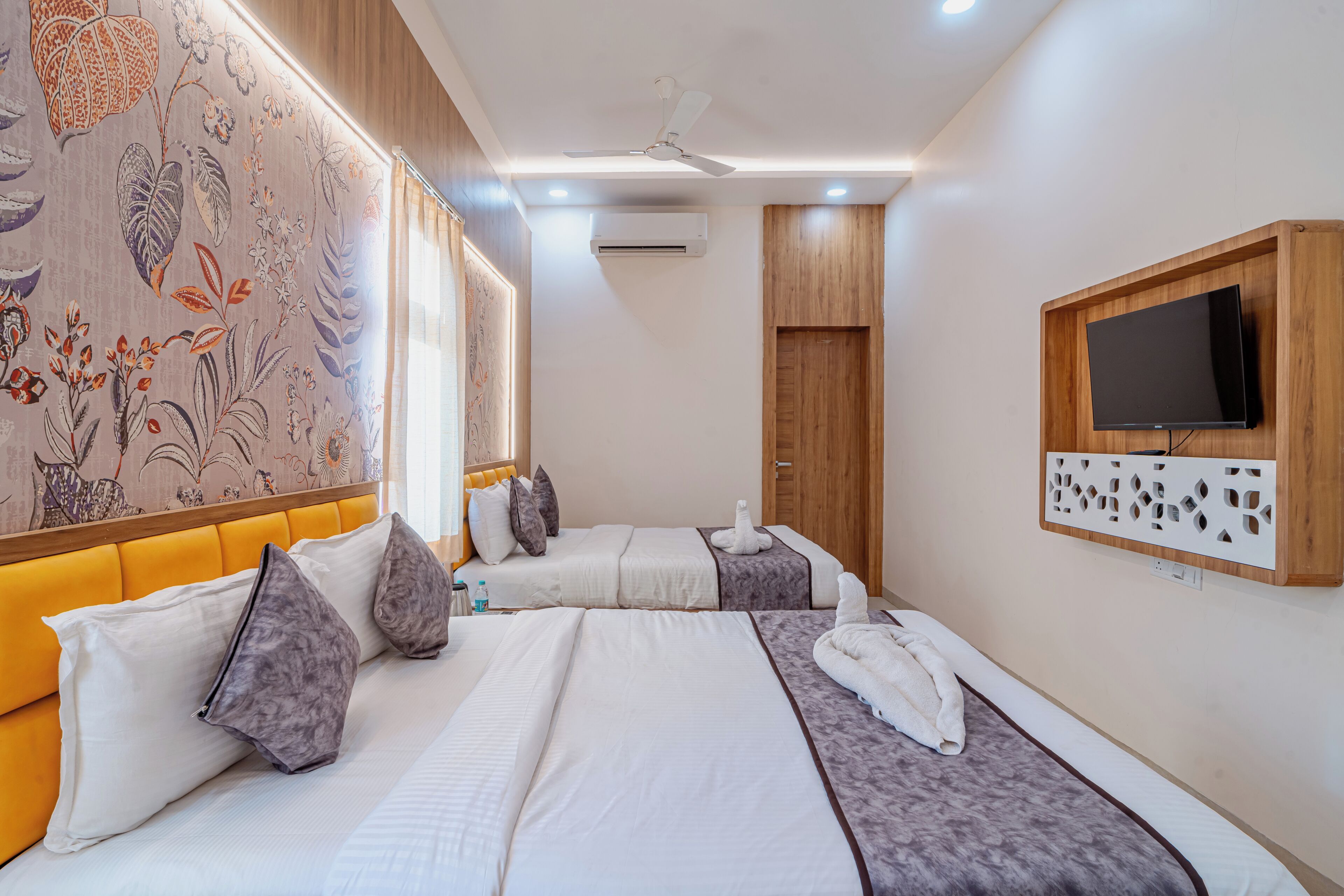 Habitación de hotel con dos camas, televisión, aire acondicionado y ventilador de techo.