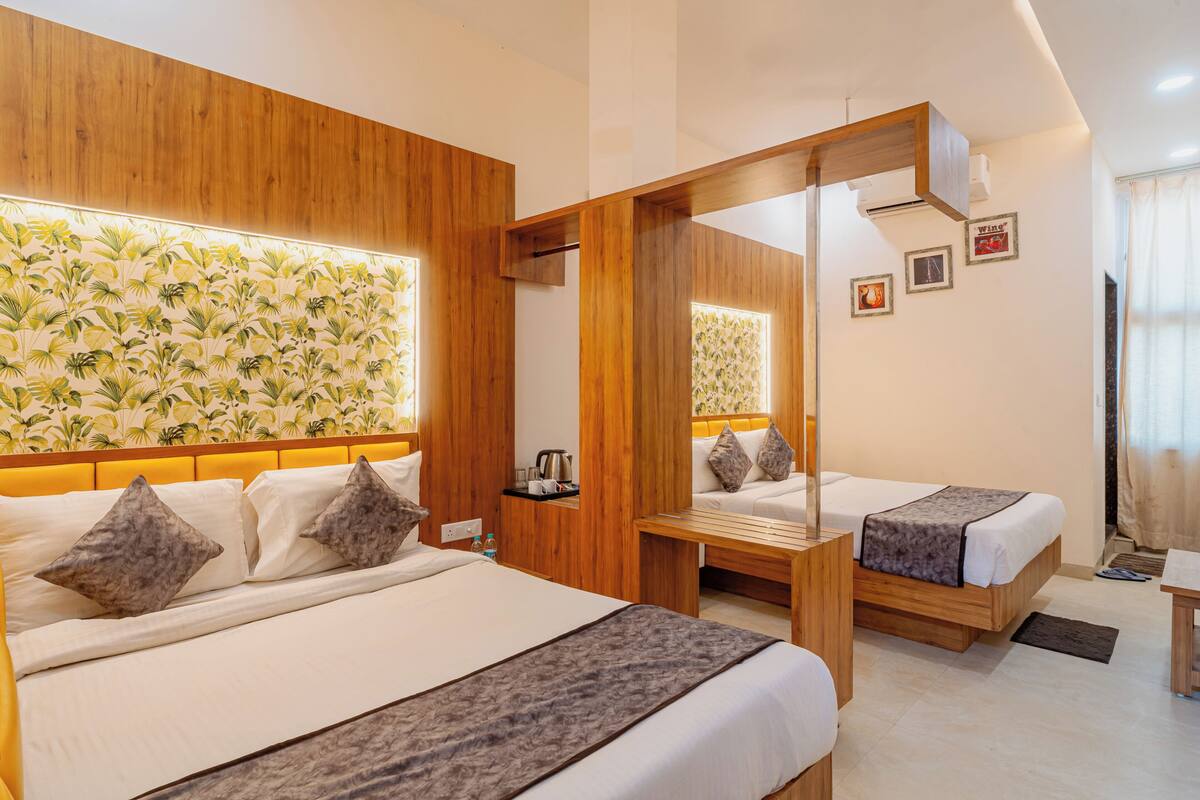 A hotel room with two beds, wooden headboards, a large window with curtains, and a wall with a tropical wallpaper design.