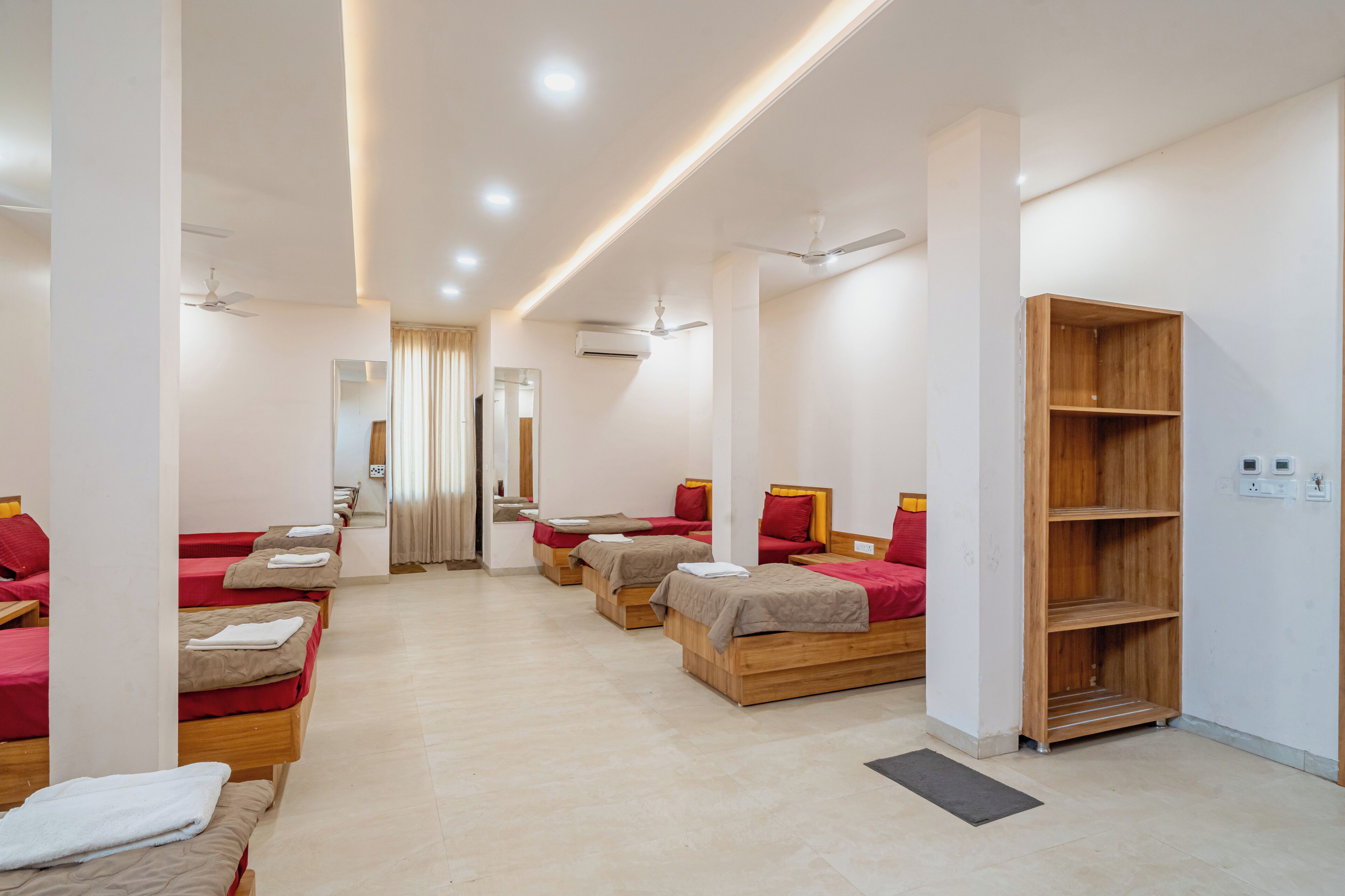 Ein Hotelzimmer mit mehreren Betten, einem Holzregal und Deckenventilatoren.