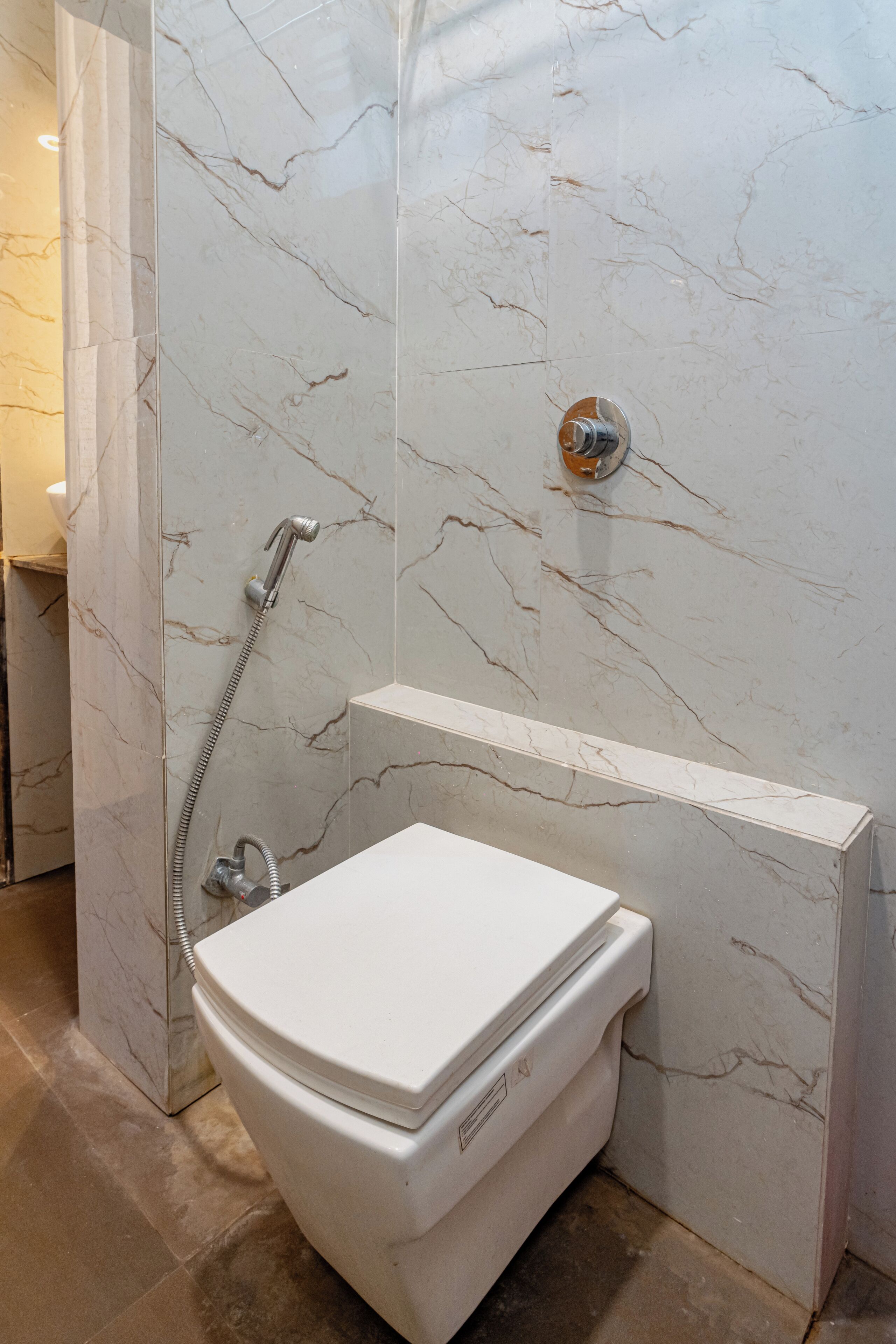 Baño con pared de mármol, ducha e inodoro.